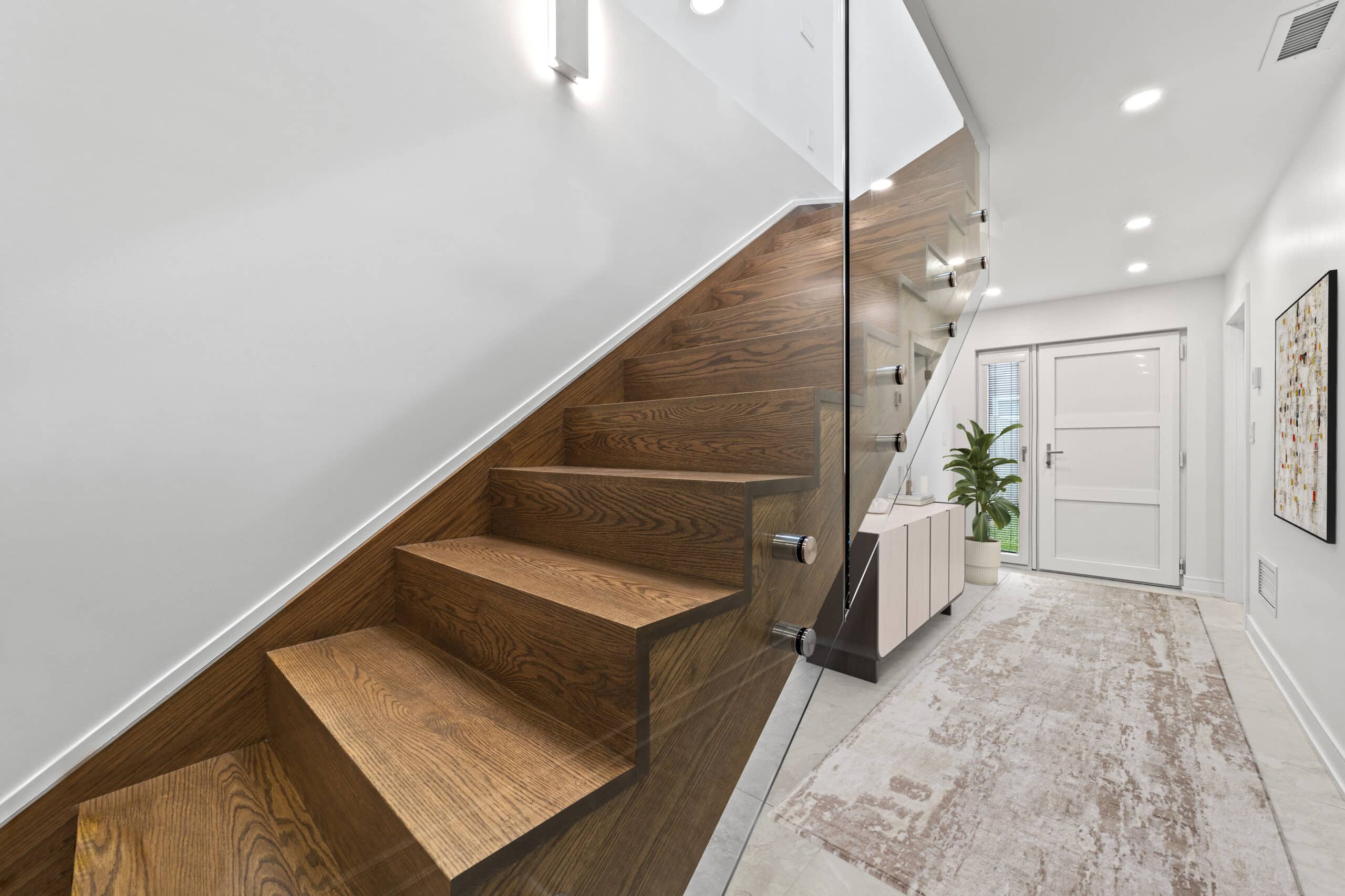 Modern entryway featuring wooden staircase, glass railing, and elegant decor